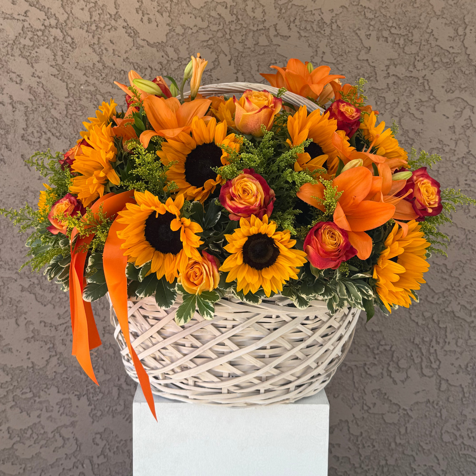 Bouquet of orange, yellow, and red flowers in a woven basket against a textured wall.