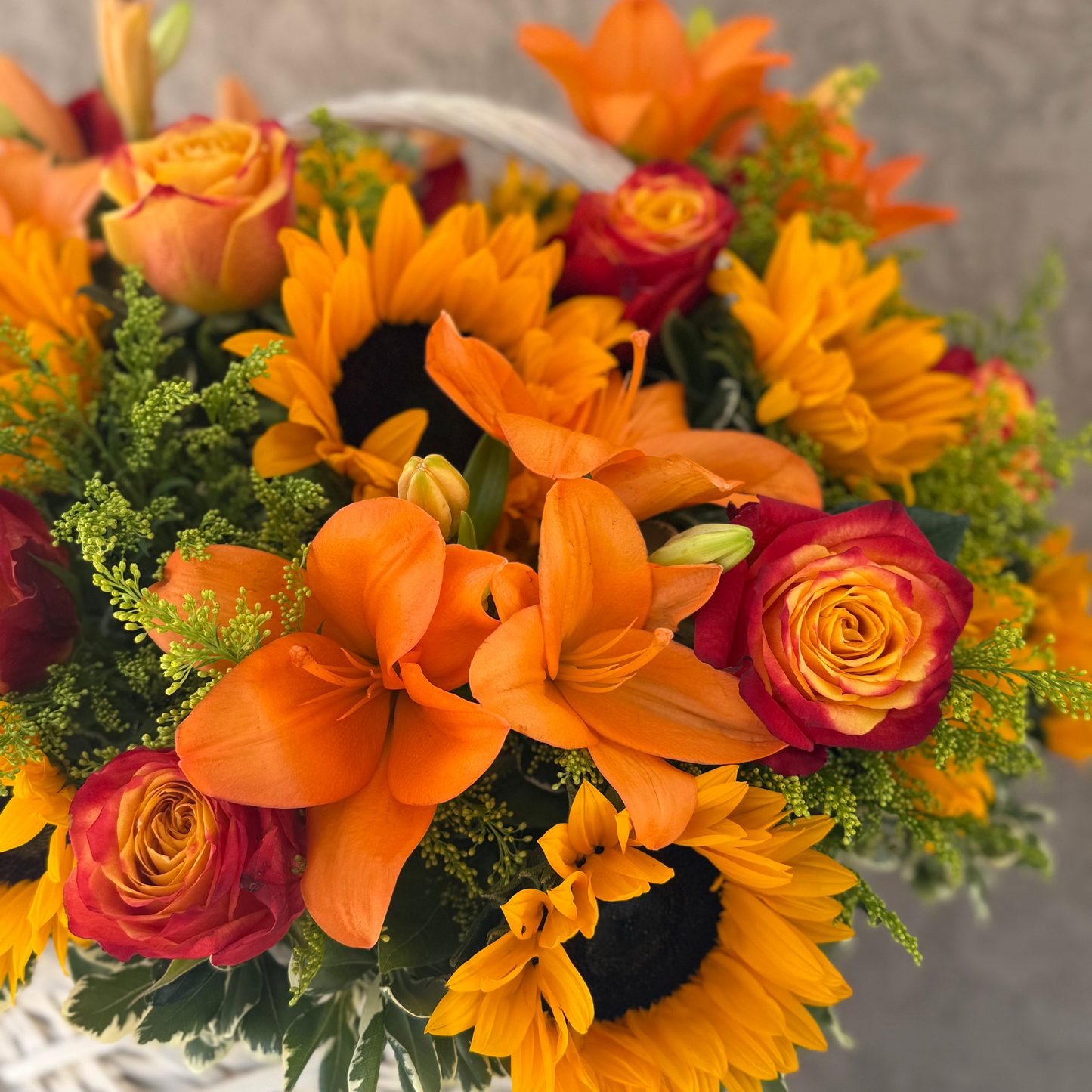 Bouquet of orange sunflowers and red roses in a white basket against a neutral background