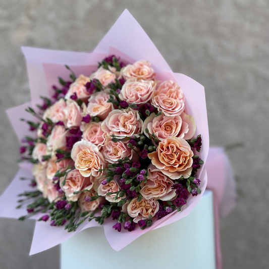 Bouquet of pink and purple flowers wrapped in paper on a light blue stand against a gray background