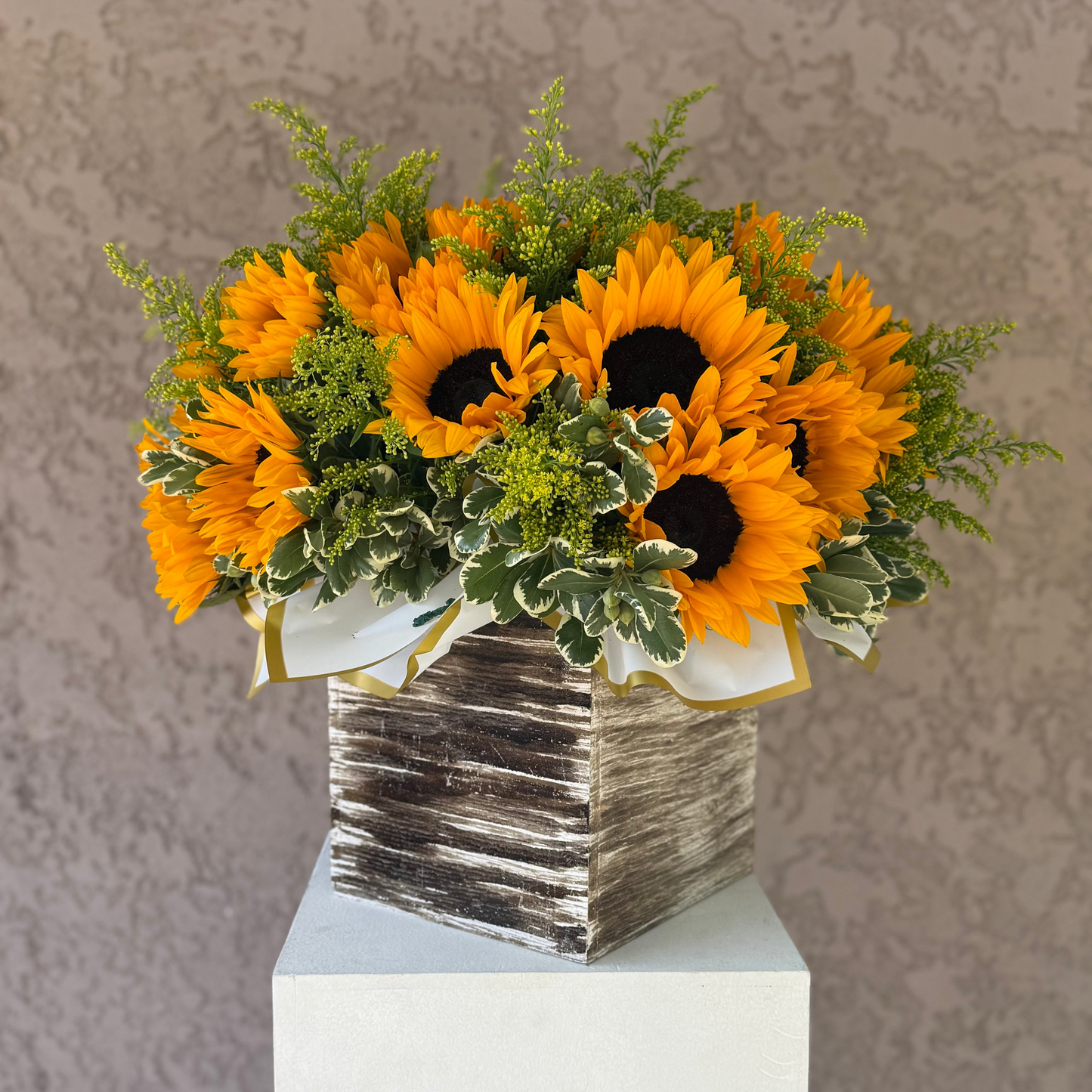 Bouquet of sunflowers in a textured vase on a white pedestal against a neutral background