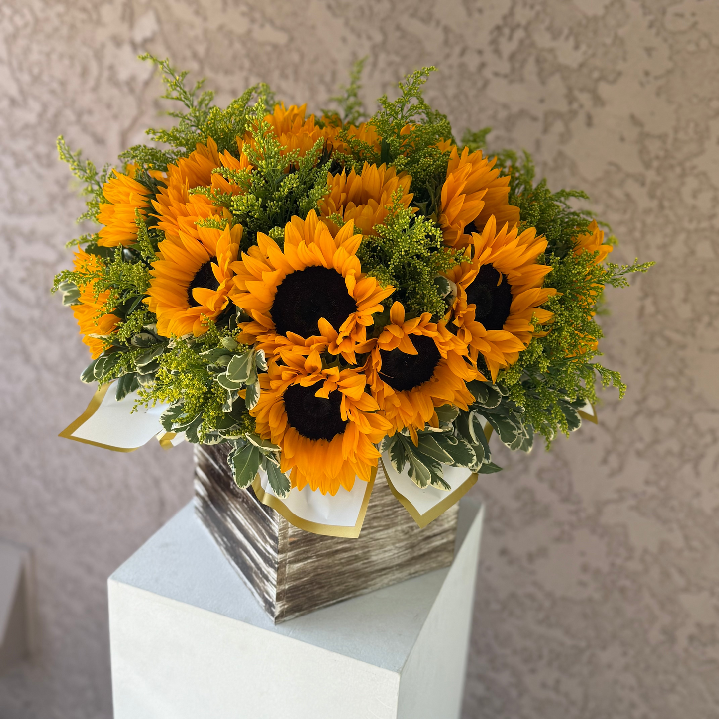 Bouquet of sunflowers in a decorative container on a pedestal against a neutral background