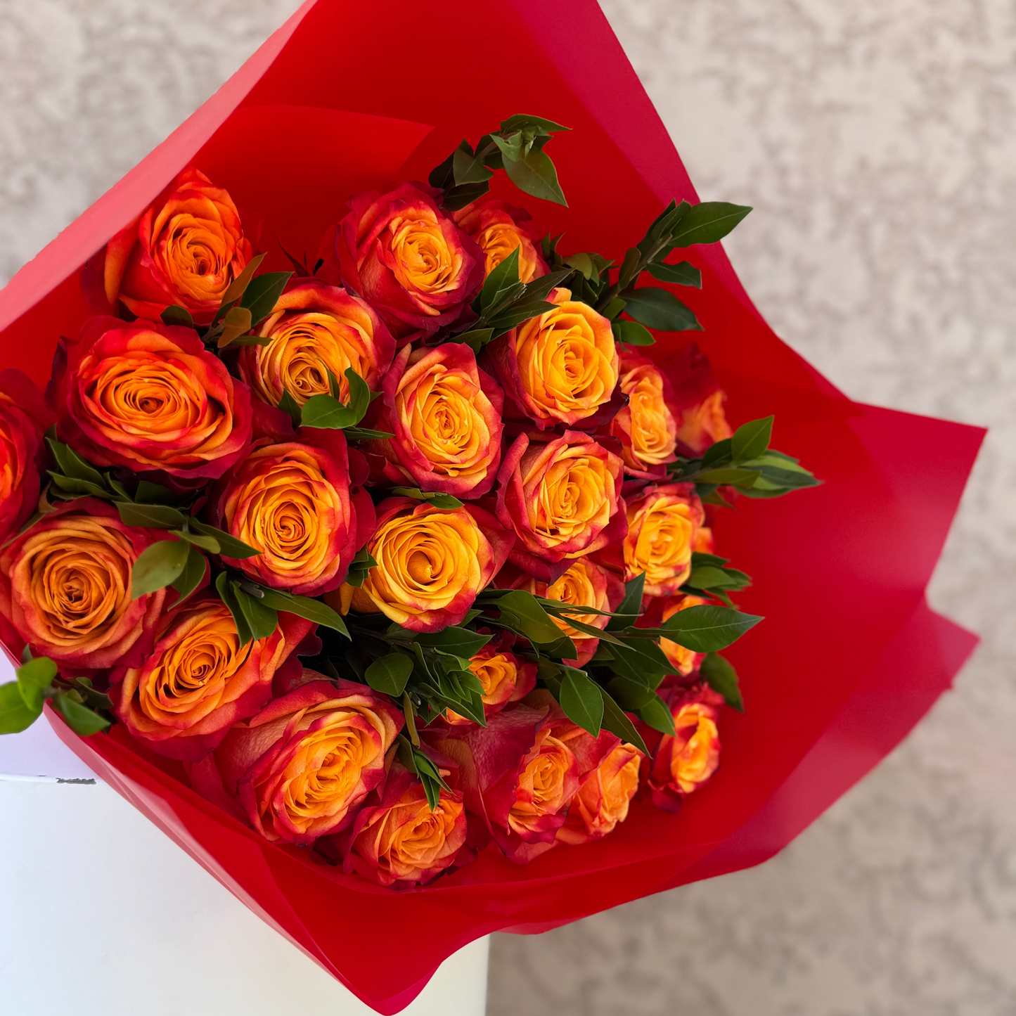 Bouquet of orange roses wrapped in red paper on a neutral background