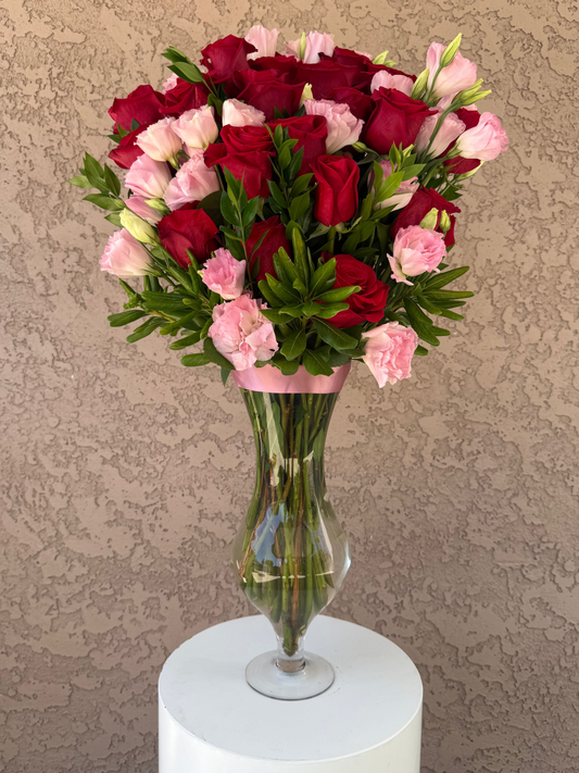 Bouquet of red and pink flowers in a clear vase on a white pedestal against a beige background