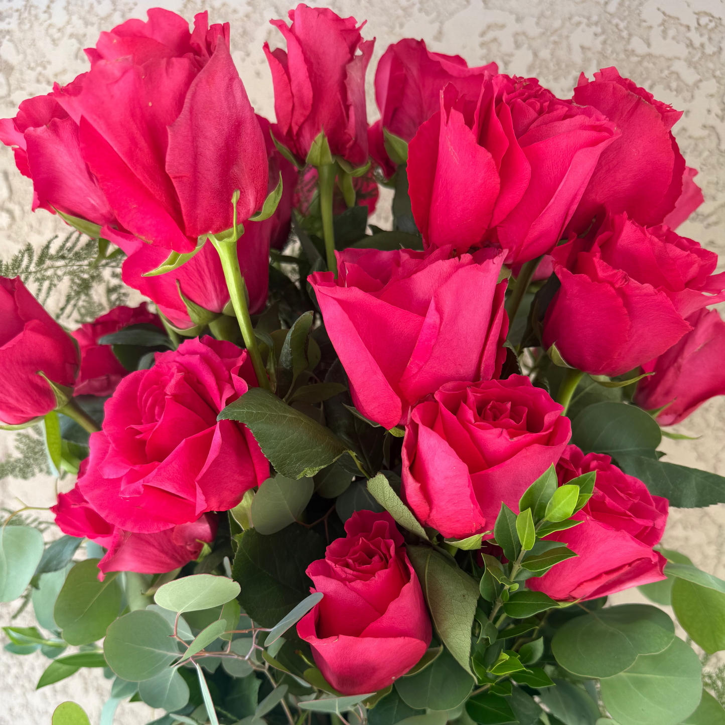Bouquet of red roses with green leaves in a clear vase against a neutral background
