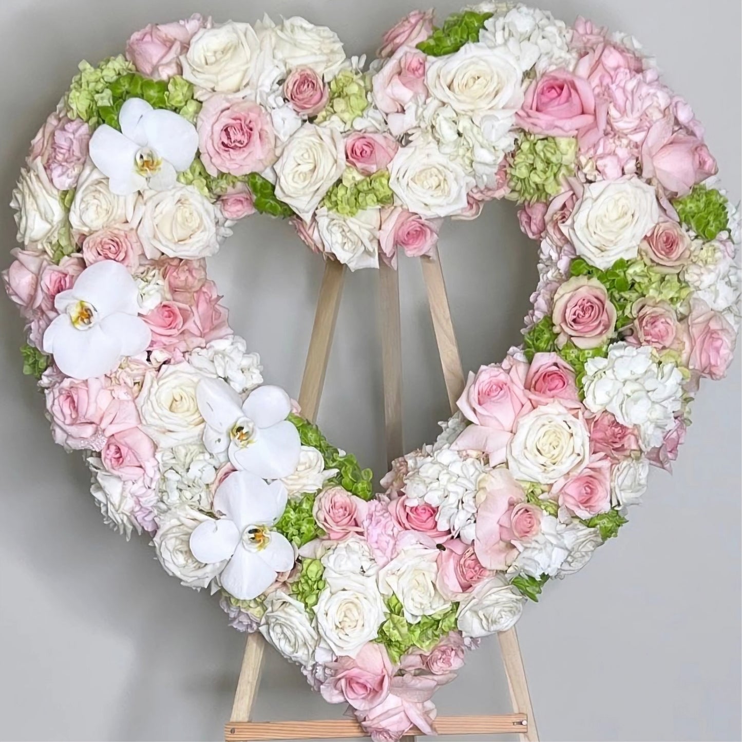 Heart-shaped floral arrangement with pink, white, and green flowers on a gray background