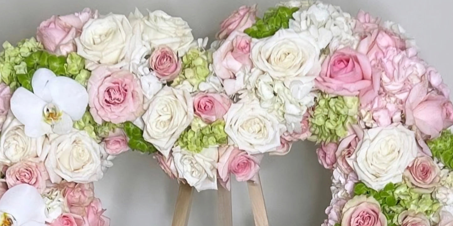 Floral arrangement shaped like a heart with pink, white, and green flowers on a gray background
