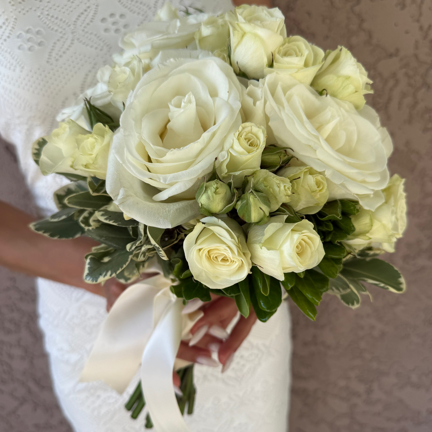 Bouquet of white roses held by a person wearing a white dress.