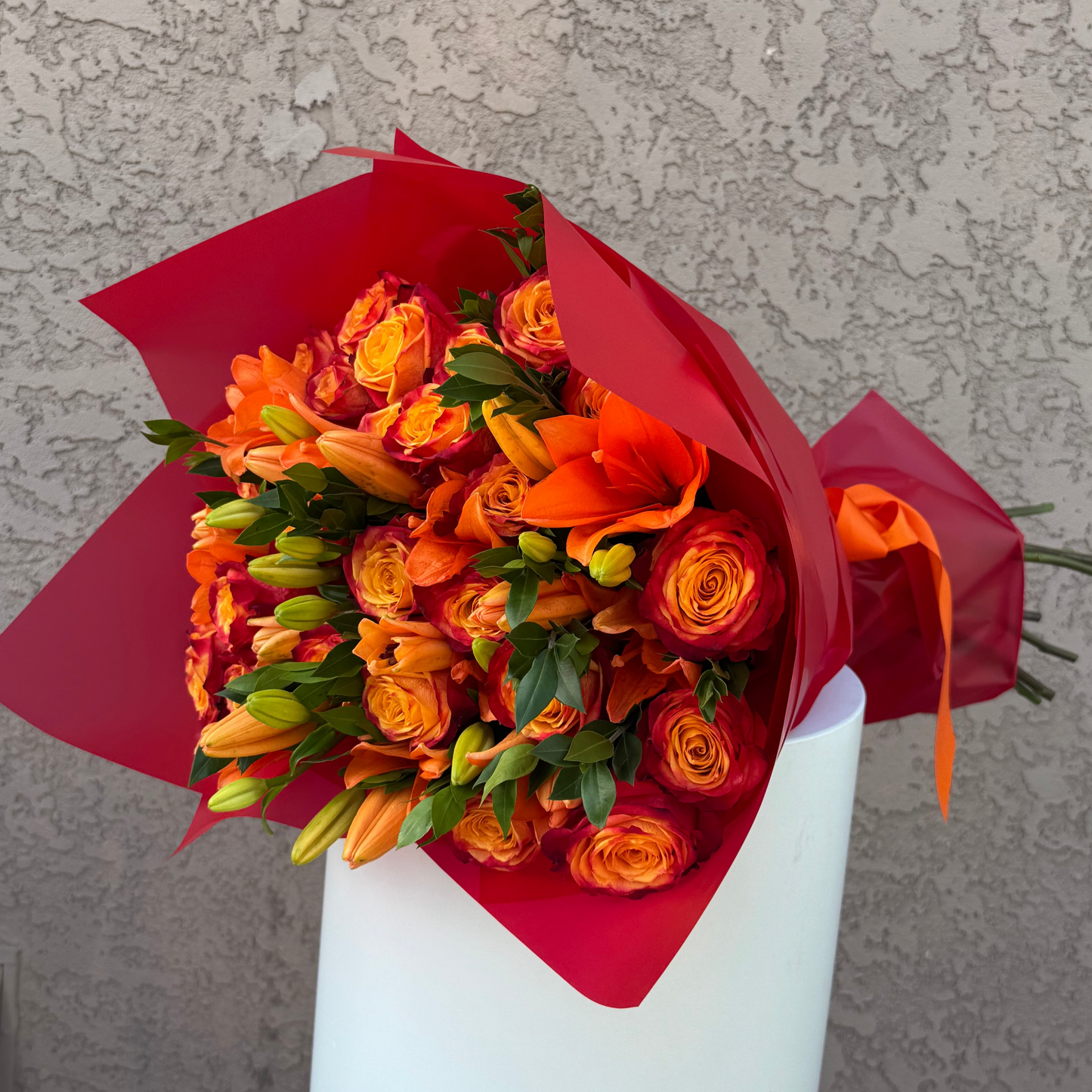 Bouquet of orange flowers wrapped in red paper on a gray background