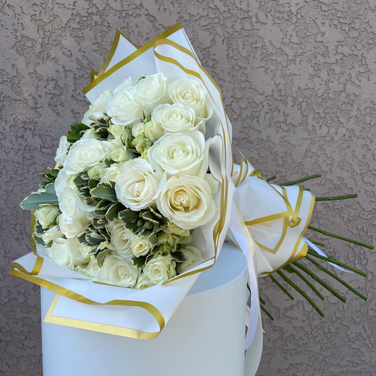 Bouquet of white roses wrapped in white paper with gold accents against a textured gray background