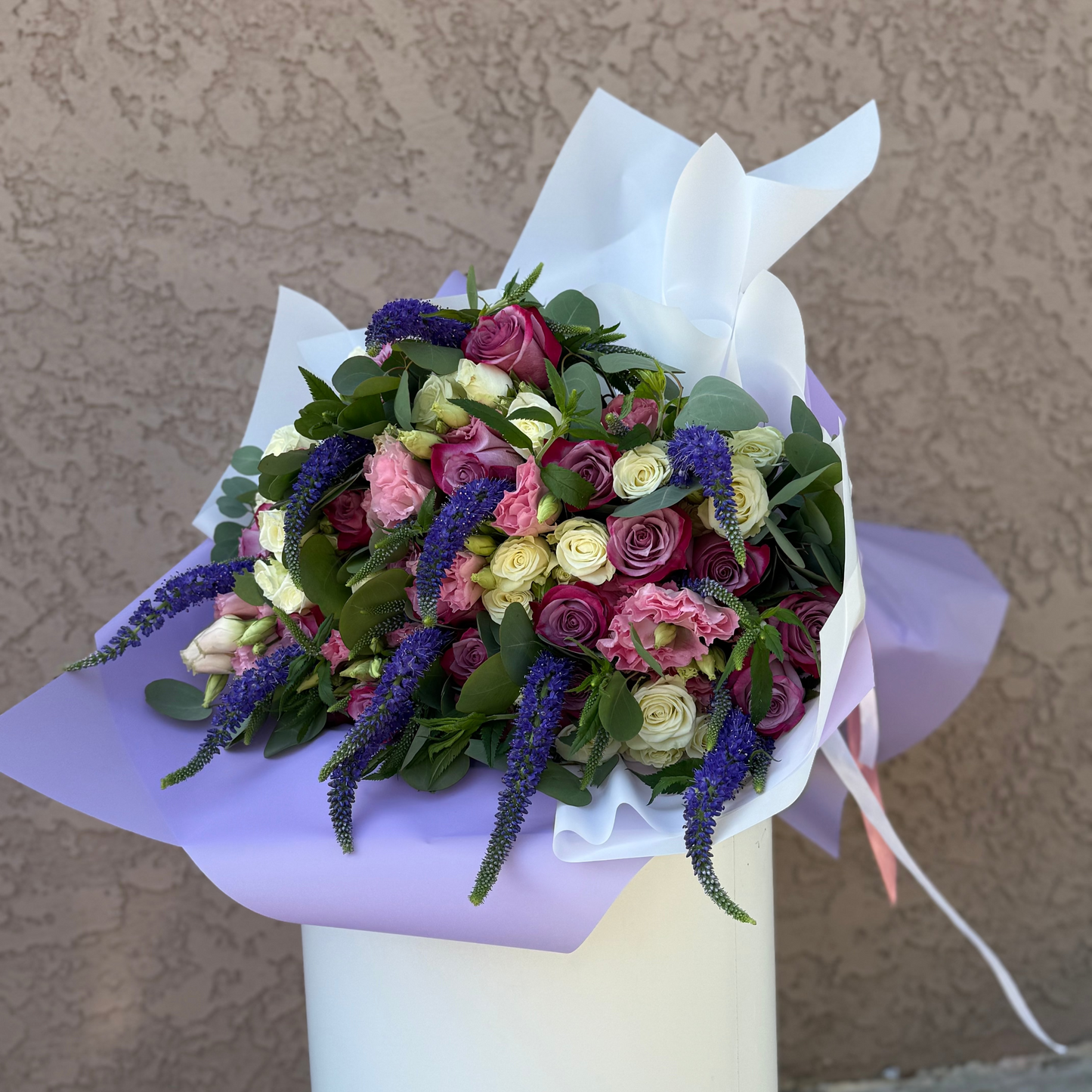 Bouquet of flowers wrapped in white paper on a stand against a beige wall.
