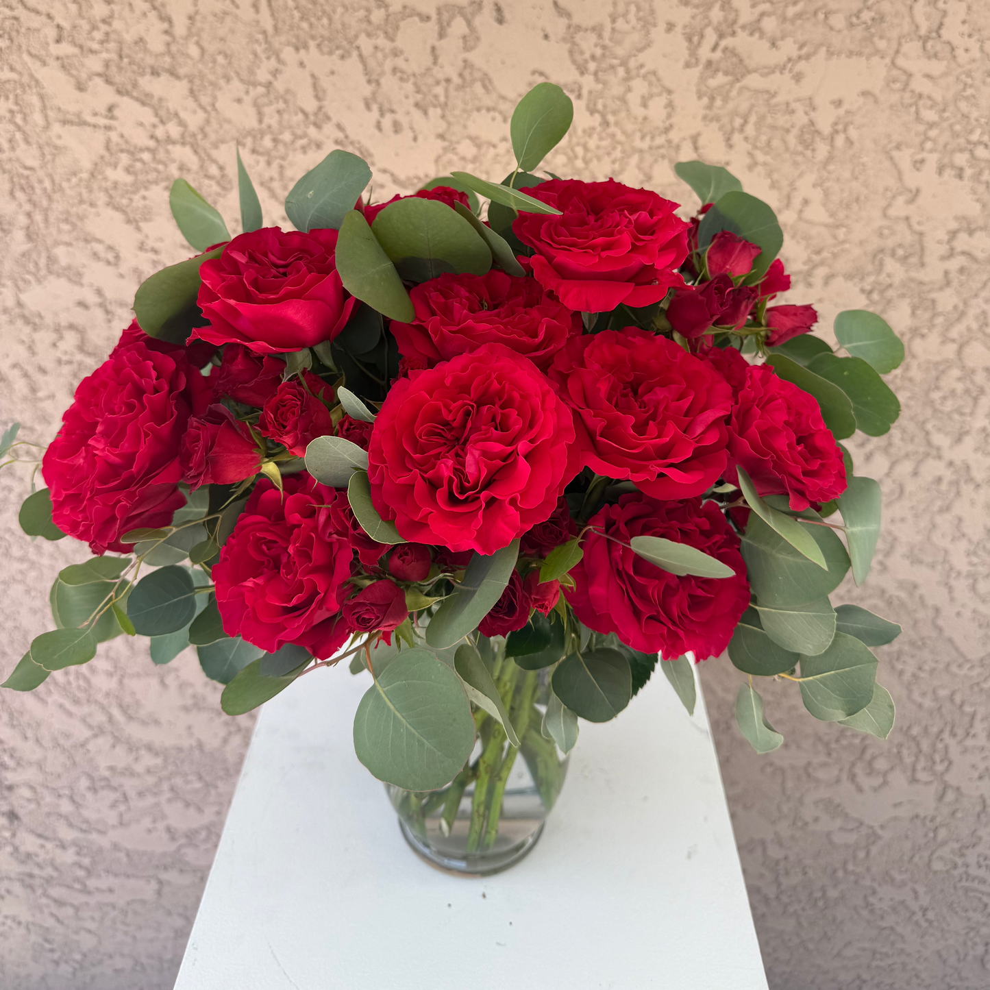Bouquet of red roses in a clear vase on a white surface with a beige textured background