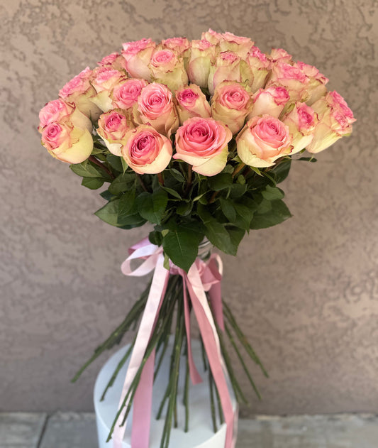 Bouquet of pink and white roses with green leaves in a white vase against a neutral background