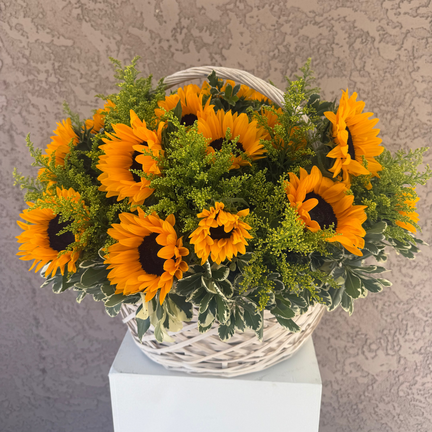 Basket of sunflowers on a white pedestal against a textured gray wall