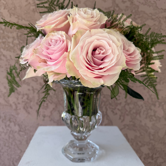Bouquet of pink roses in a clear glass vase on a white surface with a patterned wall background