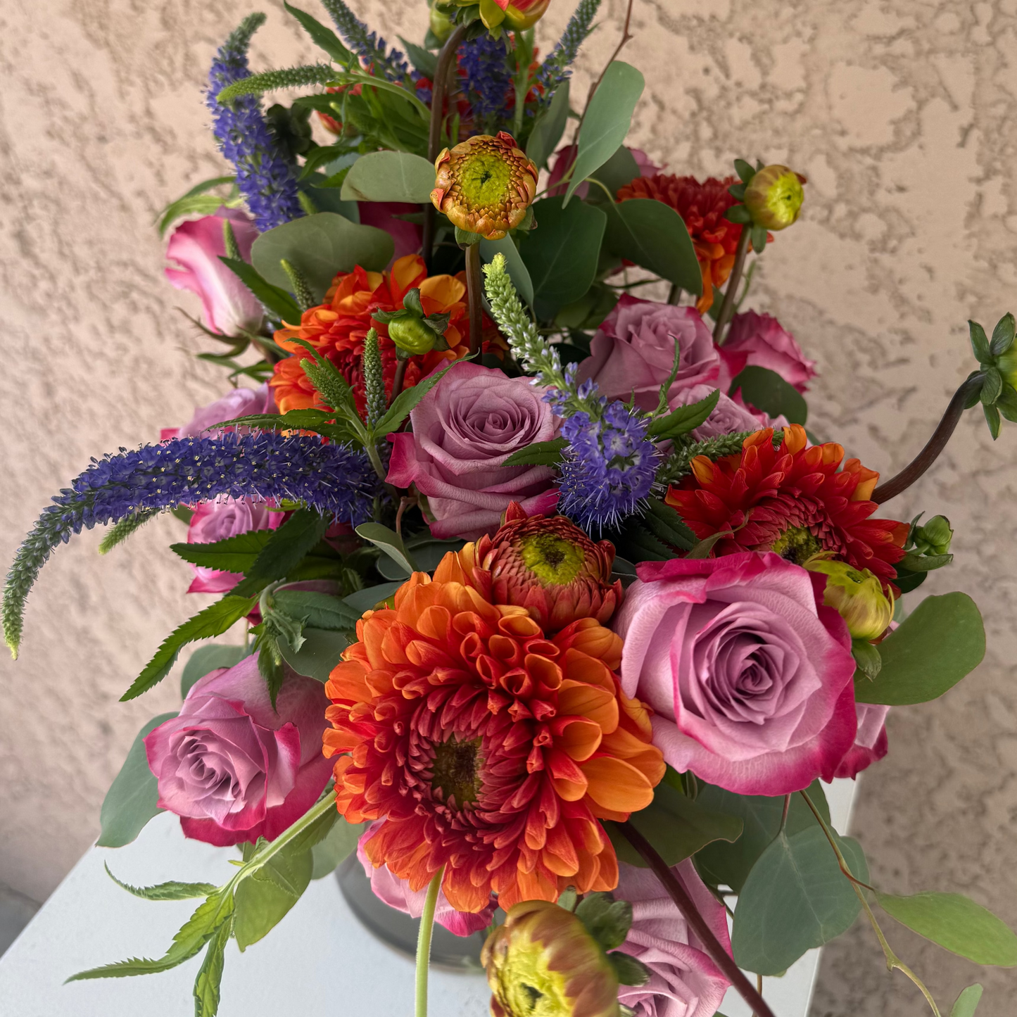 Colorful flower arrangement with pink roses, orange dahlias, and greenery on a neutral background