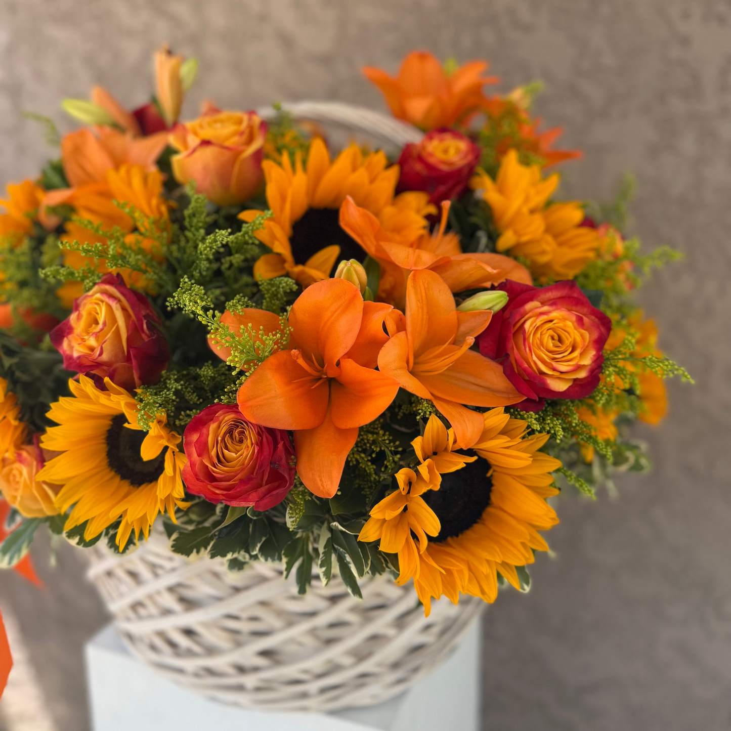 Bouquet of orange and yellow flowers in a white basket on a neutral background