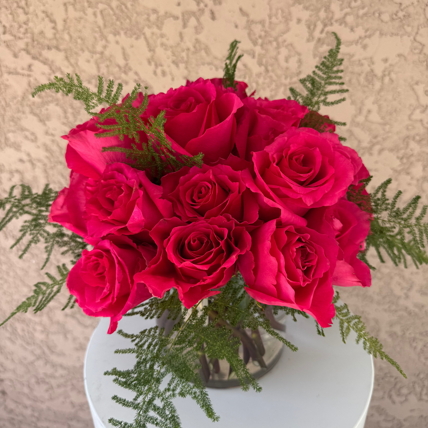 Bouquet of bright pink roses with greenery on a white pedestal against a beige background