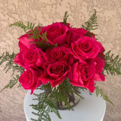 Bouquet of bright pink roses with greenery on a white pedestal against a beige background