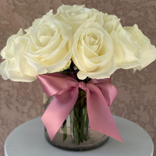 Bouquet of white roses with a pink ribbon in a clear vase on a neutral background