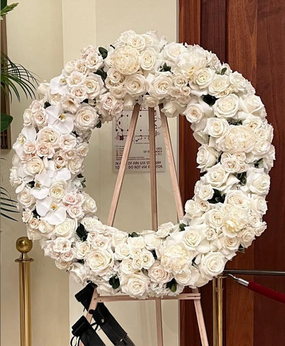 Floral wreath made of white flowers on a stand against a wooden door.