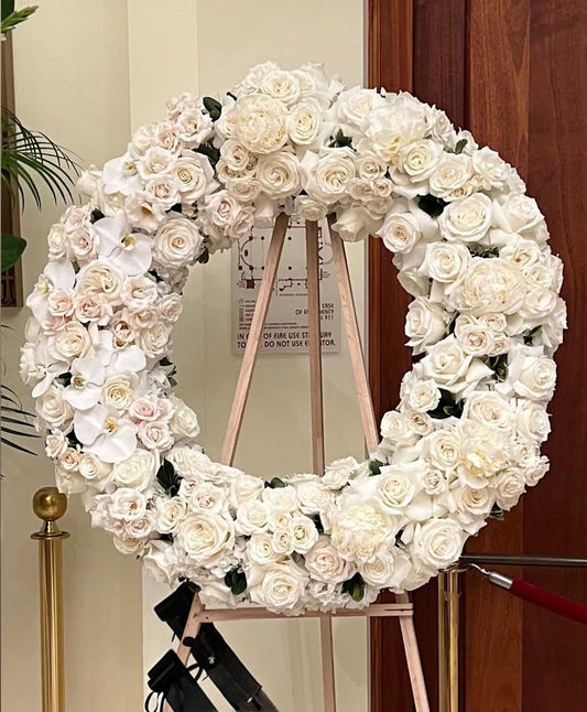 Floral wreath made of white flowers on a stand against a wooden door.