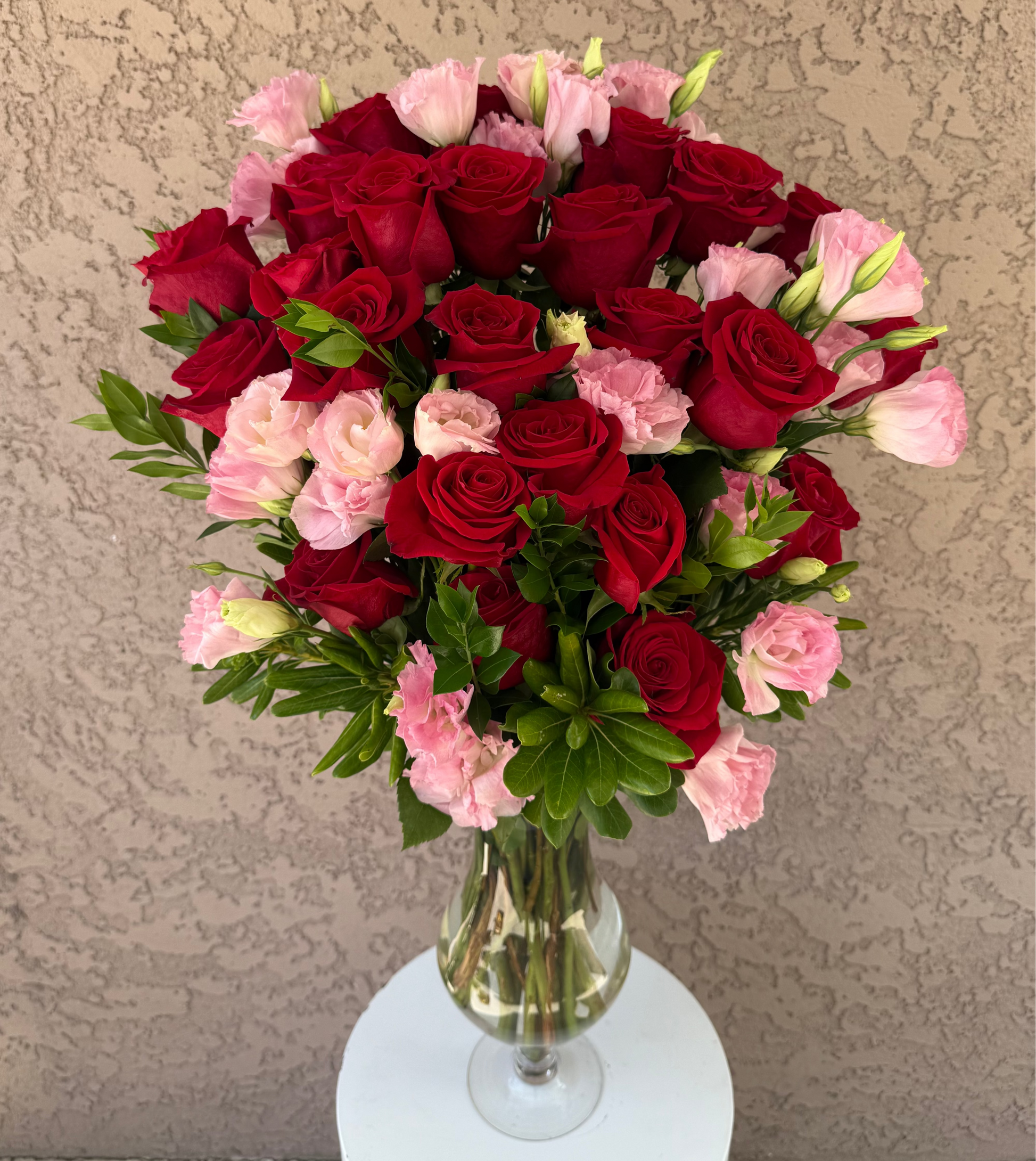 Bouquet of red and pink flowers in a clear vase on a beige background