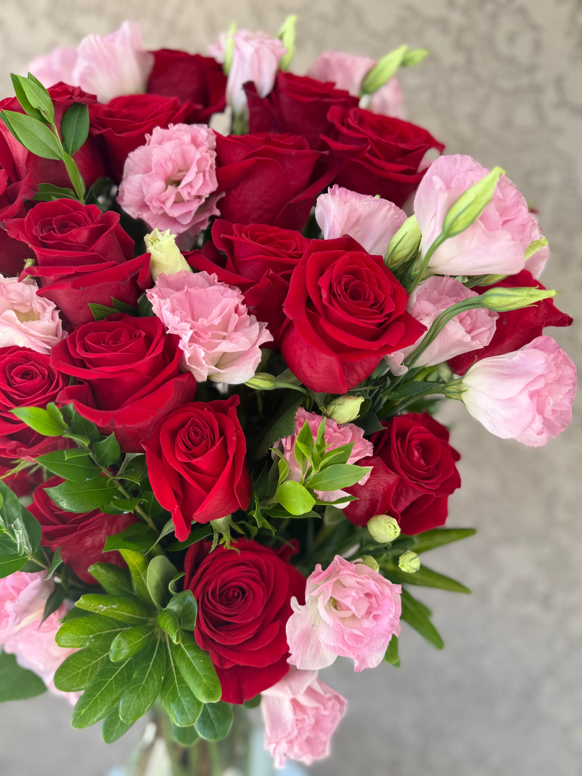 Bouquet of red roses and pink flowers with green leaves on a neutral background