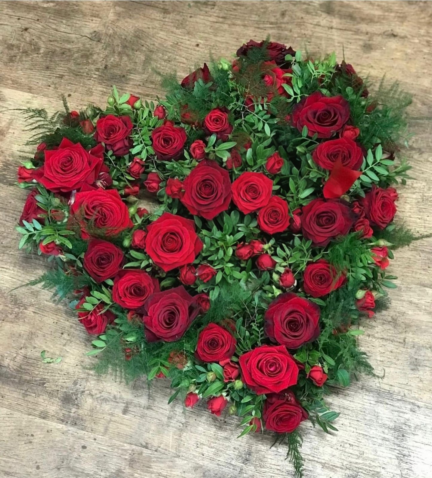Heart-shaped arrangement of red roses and greenery on a wooden surface
