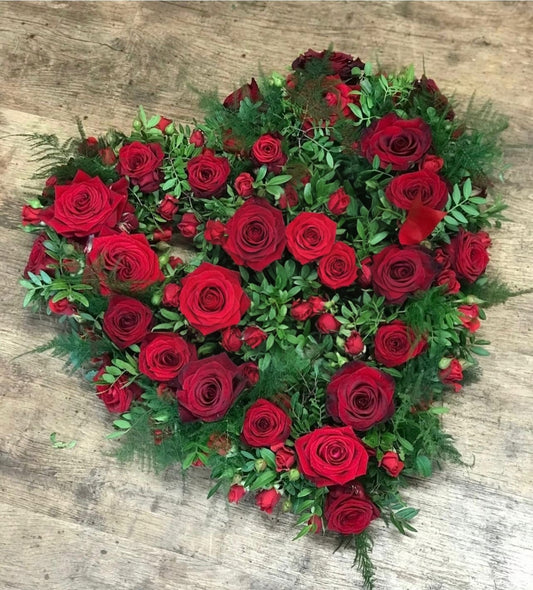 Heart-shaped arrangement of red roses and greenery on a wooden surface