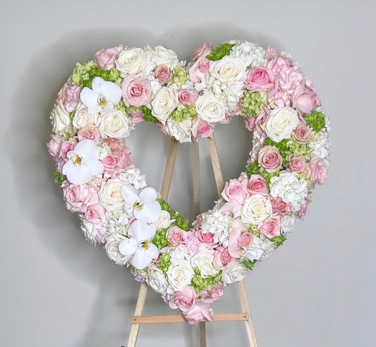 Heart-shaped floral arrangement with pink, white, and green flowers on a gray background