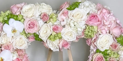 Floral arrangement shaped like a heart with pink, white, and green flowers on a gray background