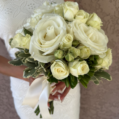 Bouquet of white roses held by a person wearing a white dress.