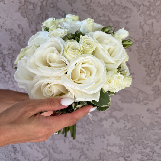 Bouquet of white roses held by a hand against a textured beige wall.