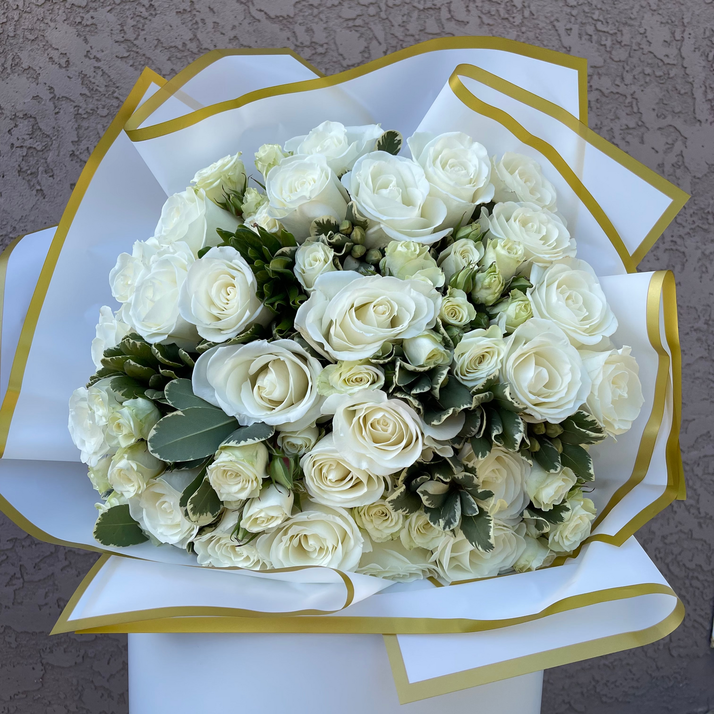 Bouquet of white roses wrapped in white paper with gold trim on a neutral background