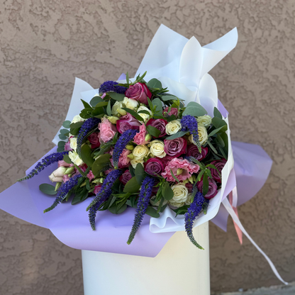 Bouquet of flowers wrapped in white paper on a stand against a beige wall.