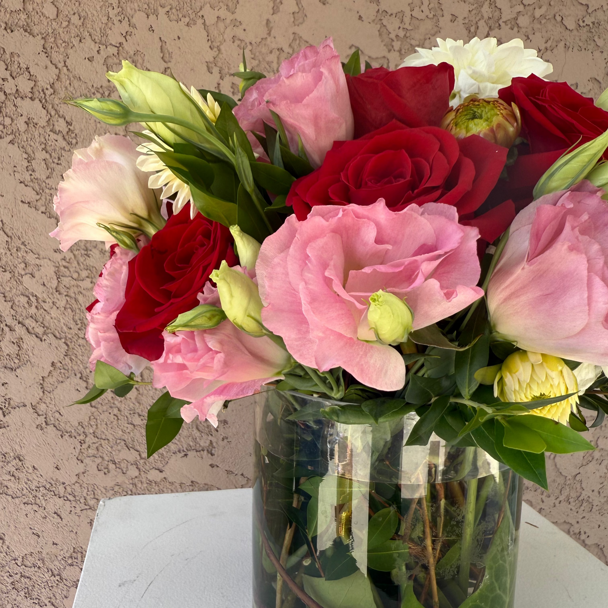 Bouquet of pink and red roses in a clear glass vase on a neutral background
