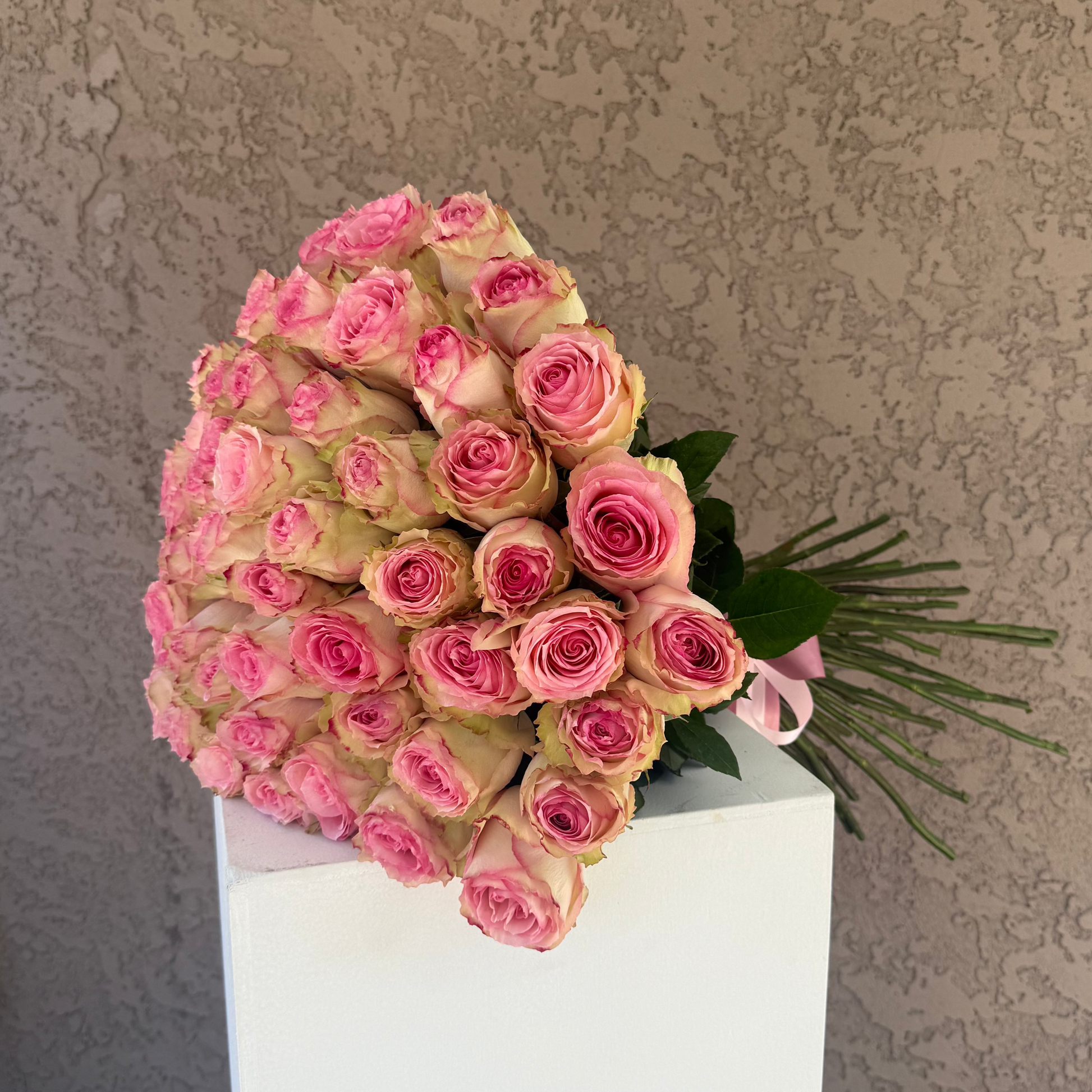 Bouquet of pink roses on a white pedestal against a textured wall.